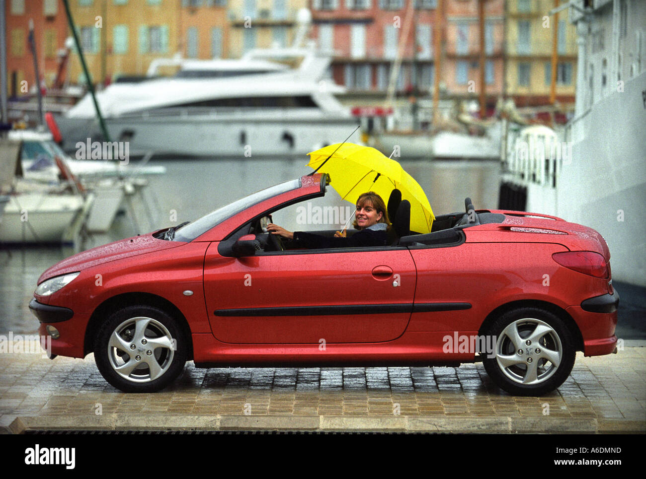 A FEMALE WITH A YELLOW UMBRELLA DRIVING A PEUGEOT 206 COUPE CONVERTIBLE  PAST ST TROPEZ HARBOUR Stock Photo - Alamy