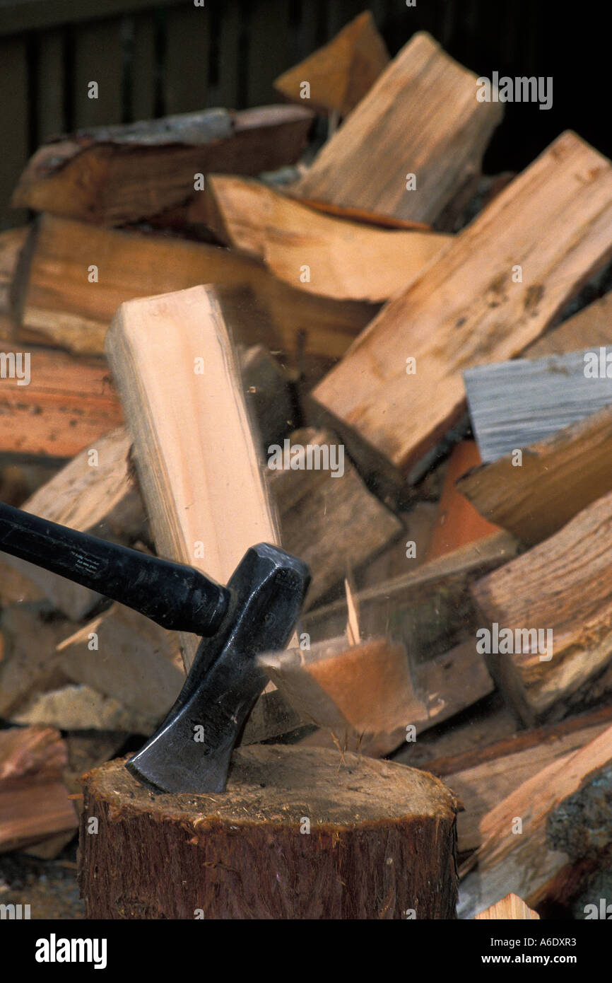 Splitting maul splits log into two pieces on chopping block with pile of split firewood Stock Photo