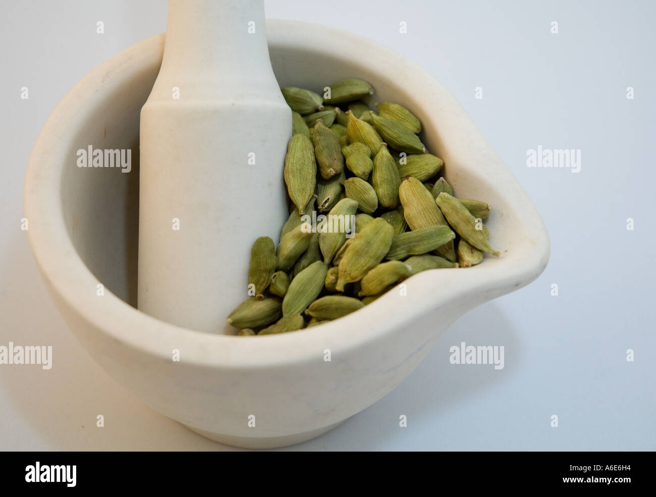 White pestle and mortar containing cardamom pods on a white background Stock Photo
