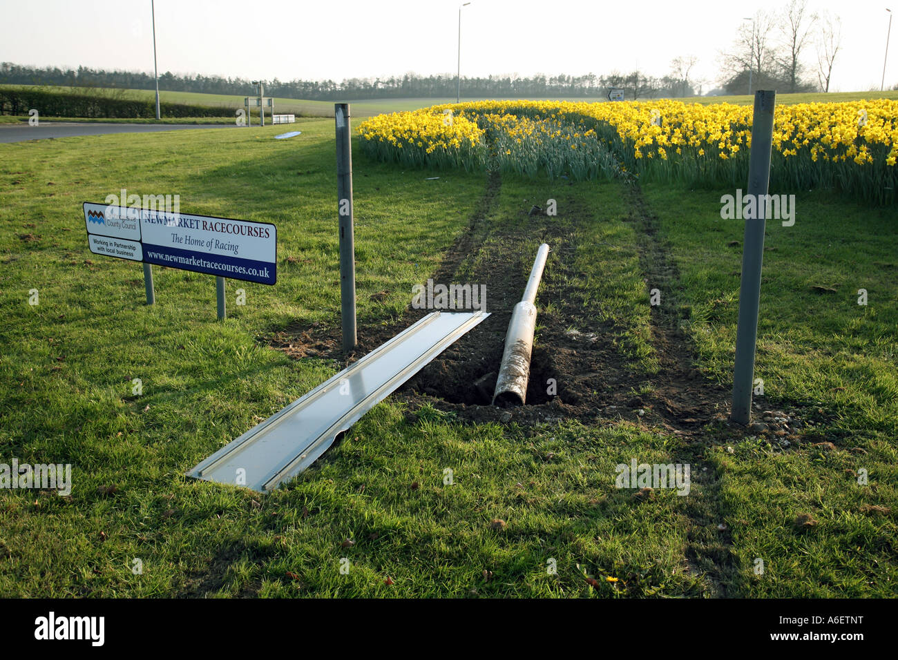 Destroyed sign and plants from accident on roundabout with 'Racecourse' sign next to it, Newmarket, Suffolk, England Stock Photo