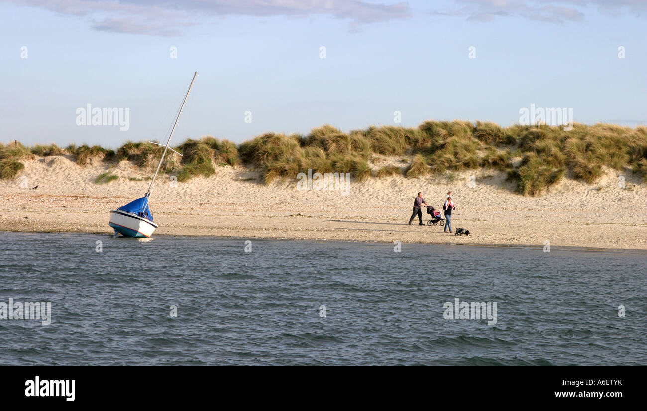 Family walking on beach UK - A family walk past a moored yacht in the evening, East Head beach, Chichester Sussex UK Stock Photo