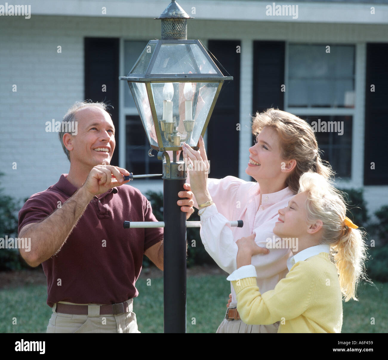 family of three installing carriage lamp in front yard Stock Photo