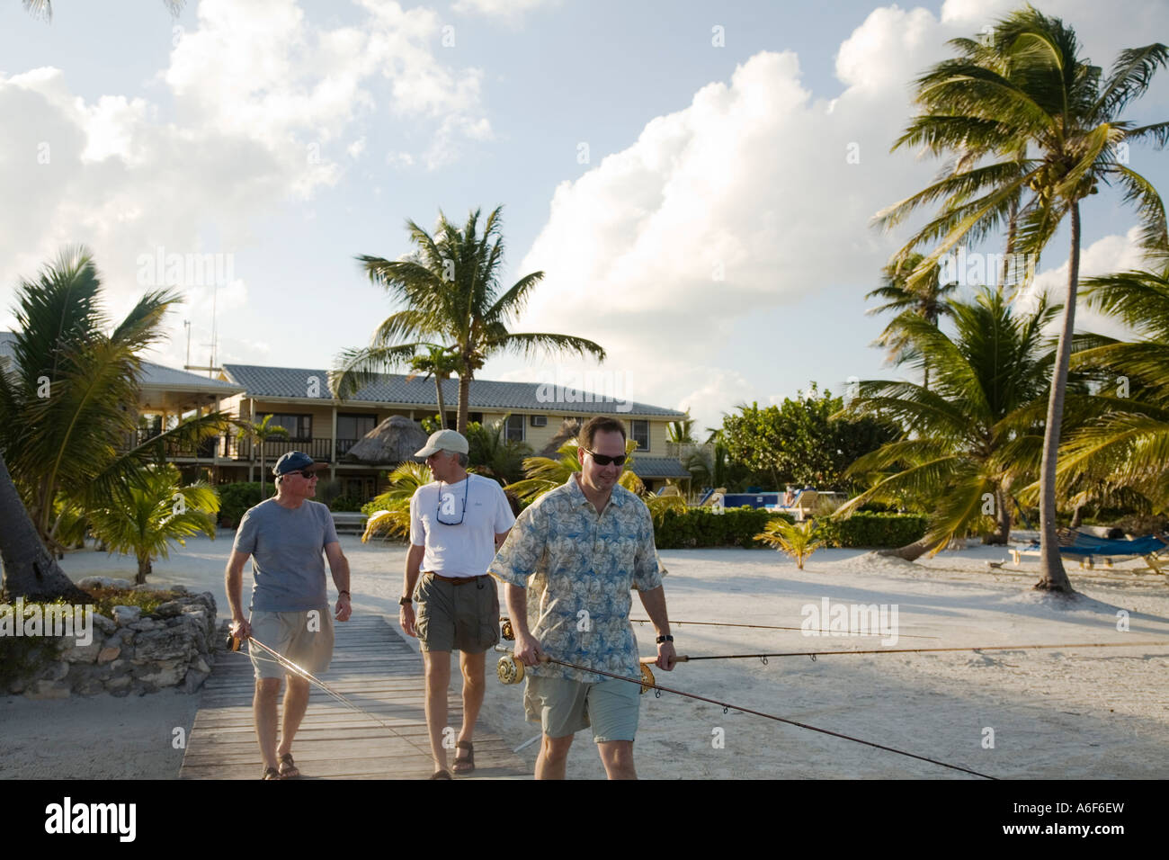 BELIZE Ambergris Caye Three adult males walk down dock to practice fly fishing from dock and casting platform Caribbean resort Stock Photo