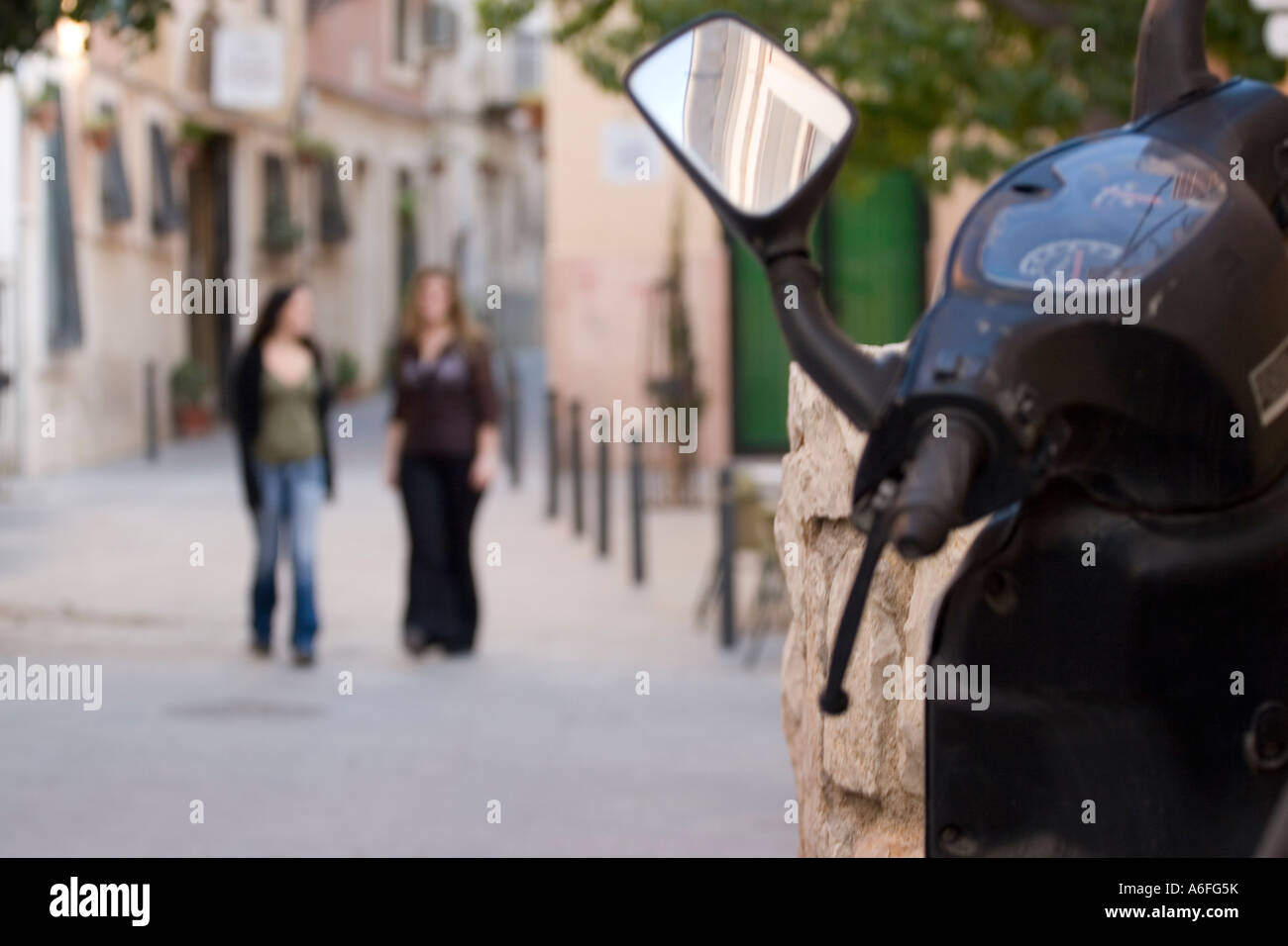 Two young women walking along Spanish street with mo-ped in foreground. Stock Photo