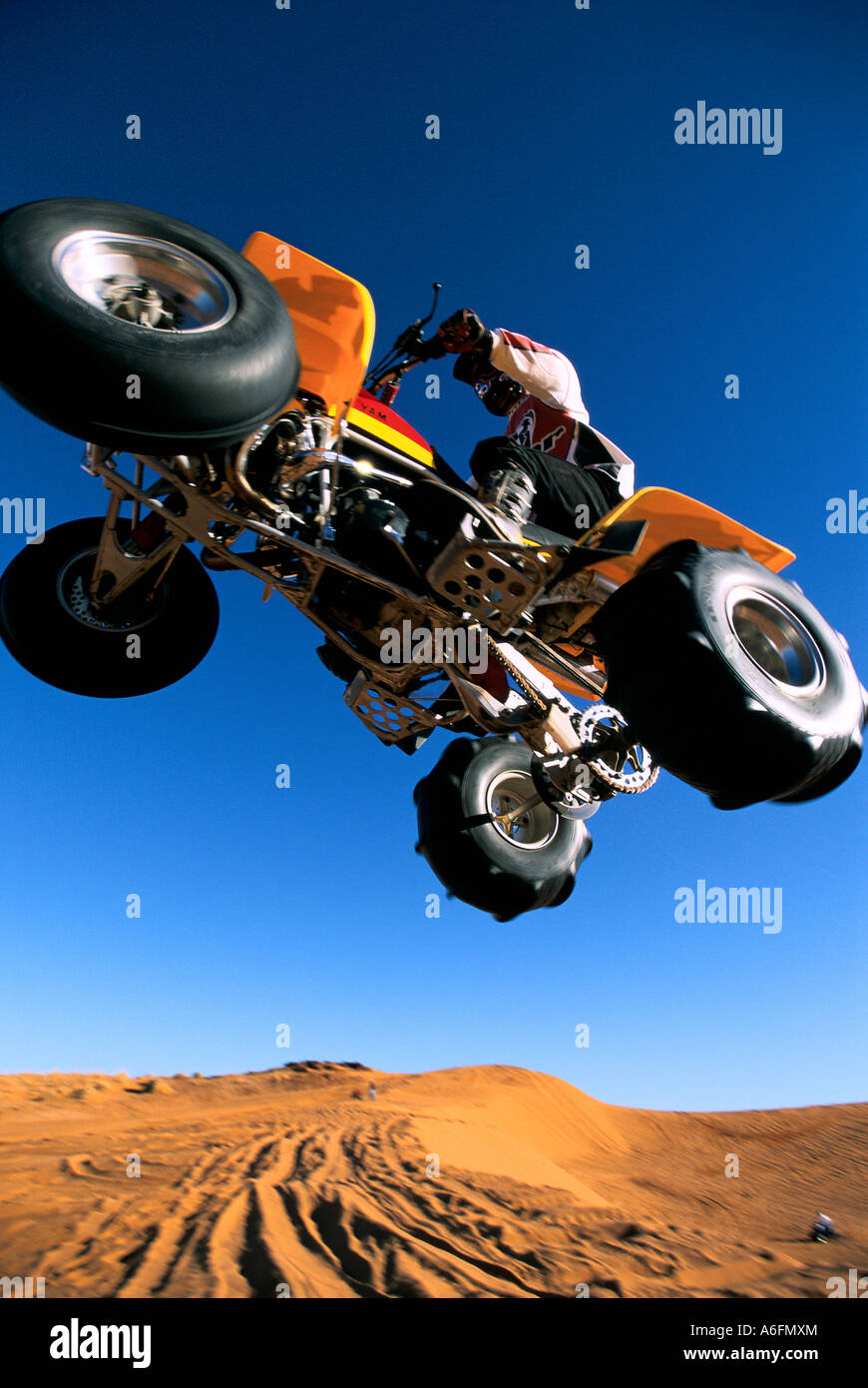 Yellow four wheeled ATV in mid air jumping Hurricane Sand Dunes