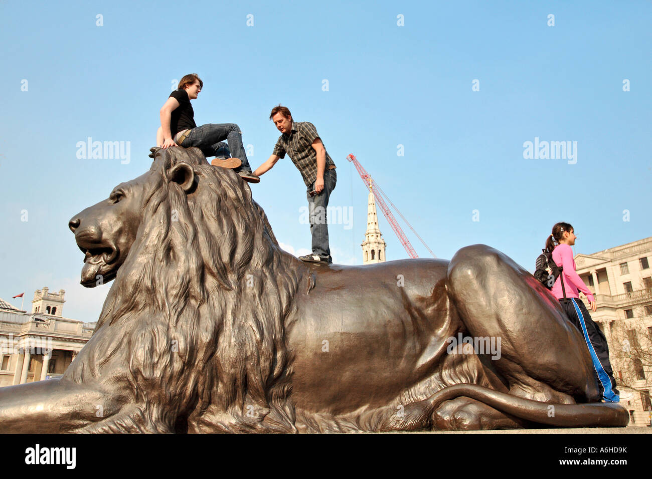 Tourists climb one of the Lion statues in trafalgar Square London Stock