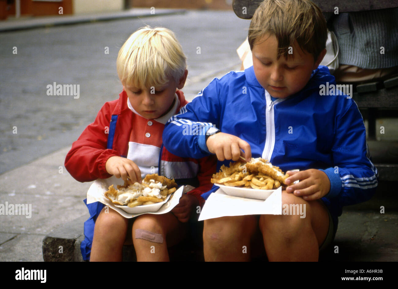 Two young lads enjoying a fish and chip meal out of paper in the street Stock Photo