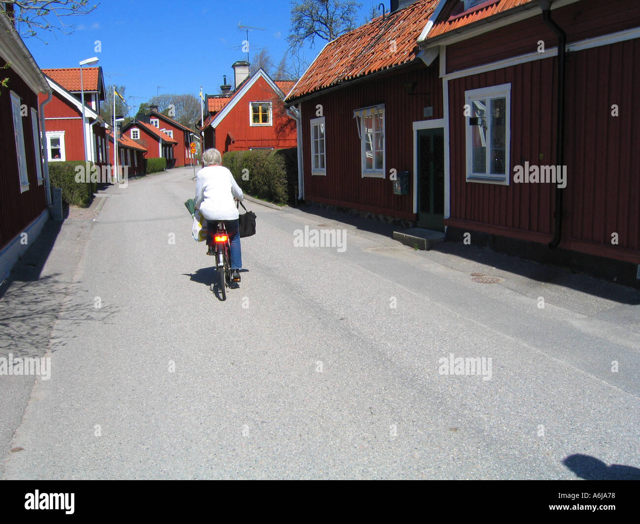 A bicyclist pedalling the street between typical Swedish red wooden houses in the idyllic small town of Trosa south of Stockhol Stock Photo