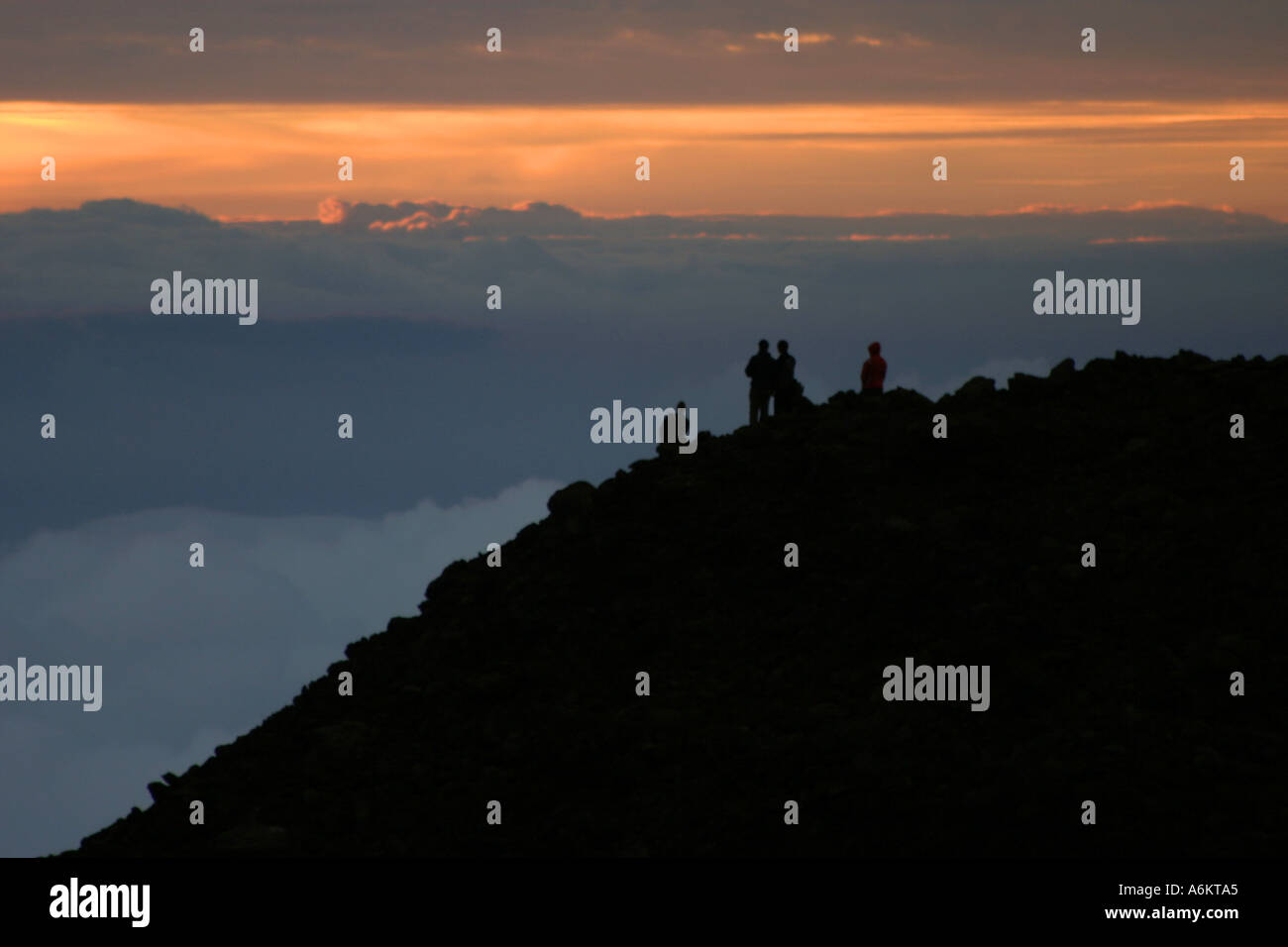 Silhouettes of four people watching sunrise from above the clouds at