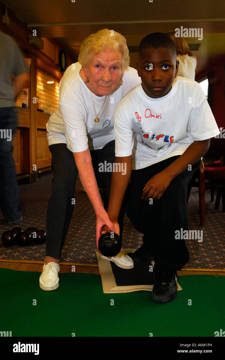 Elderly woman showing young schoolboy how to play indoor bowls London Stock Photo