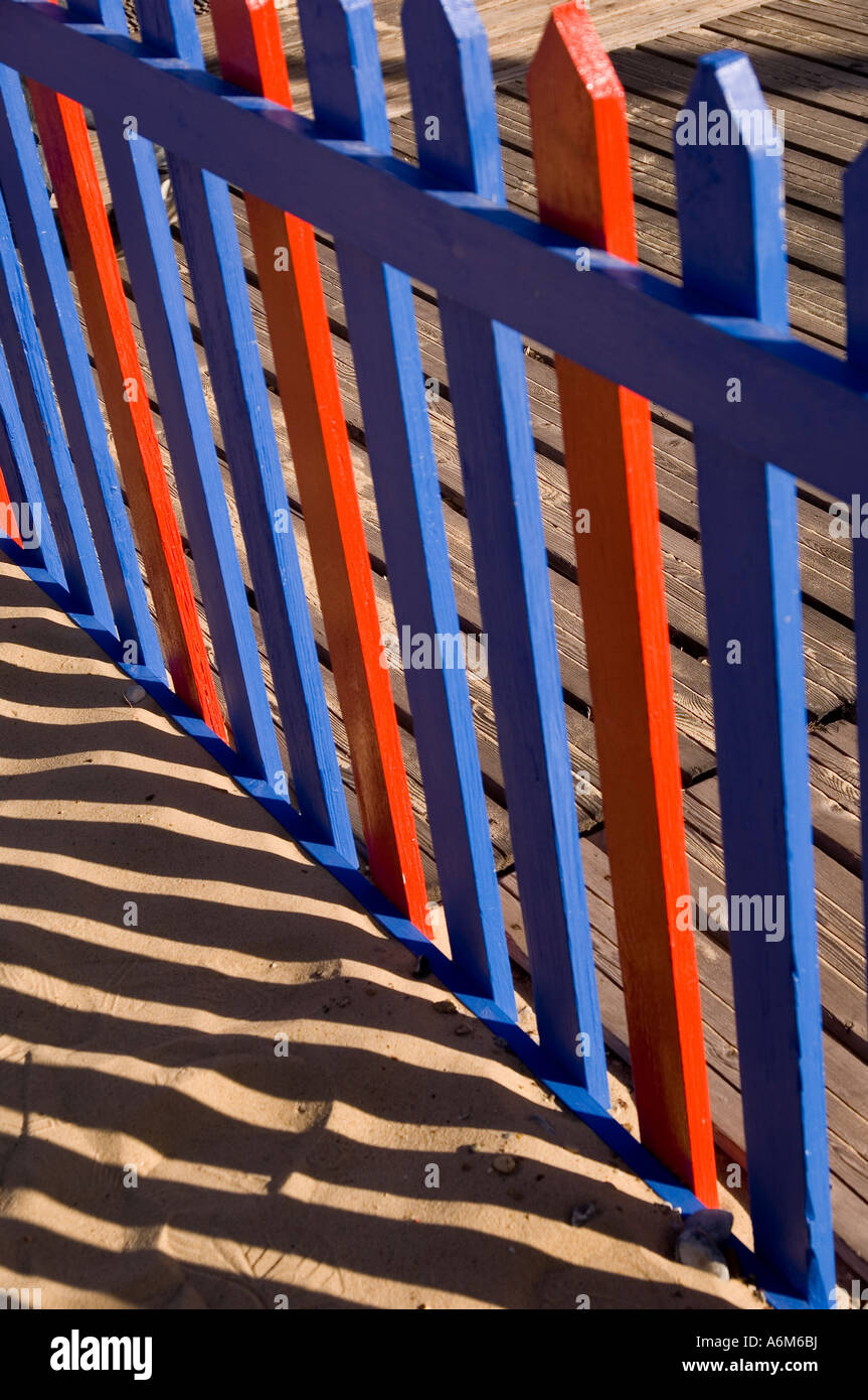 Red and Blue wooden fence with dramatic shadow cast onto the sand behind. Shot in Great Yarmouth, Norfolk UK. Stock Photo