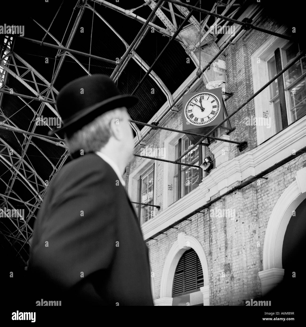 British businessman in bowler hat looking at clock at railway station Stock Photo