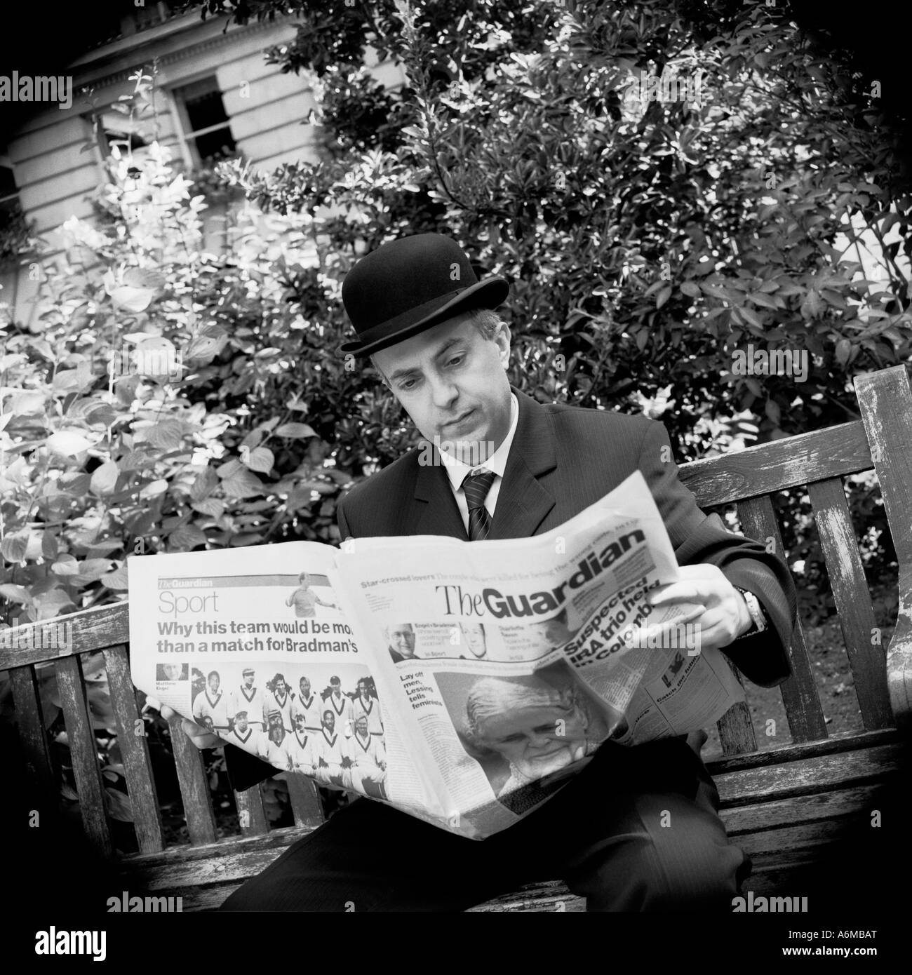 English city gent businessman reading the Guardian Newspaper on park bench Stock Photo