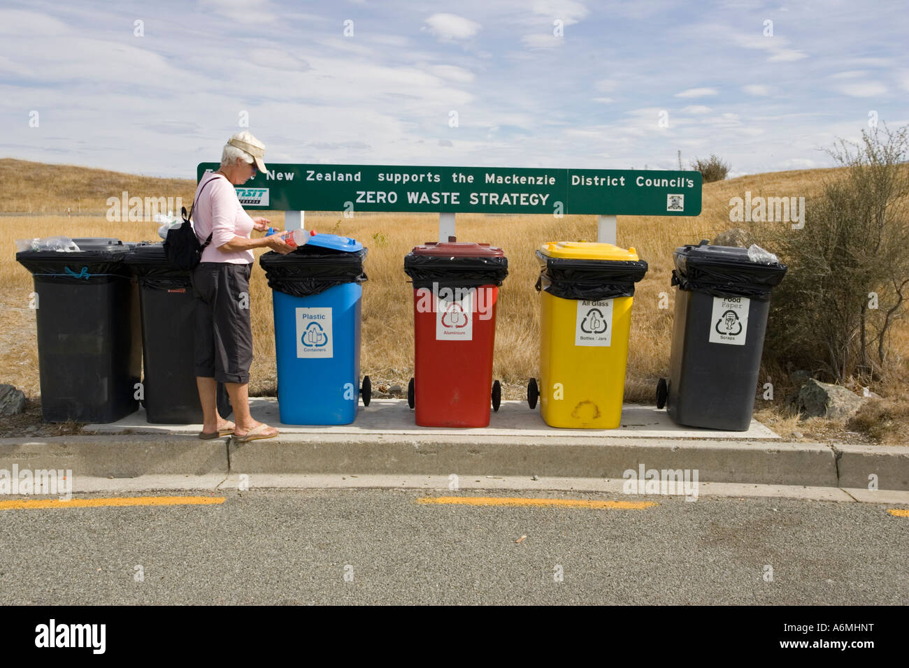 Tourist placing plastic bottle in colourful recycling bins at visitor centre near Lake Pukaki