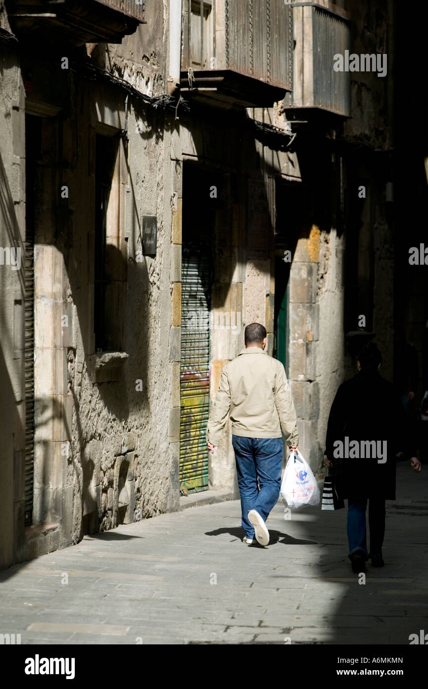 Rear view of two people with shopping bags walking down street El Barri ...