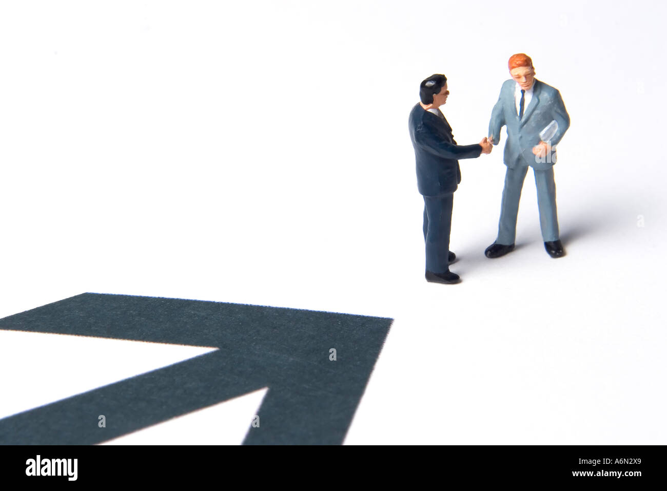 Business figurines shaking hands next to an arrow Stock Photo