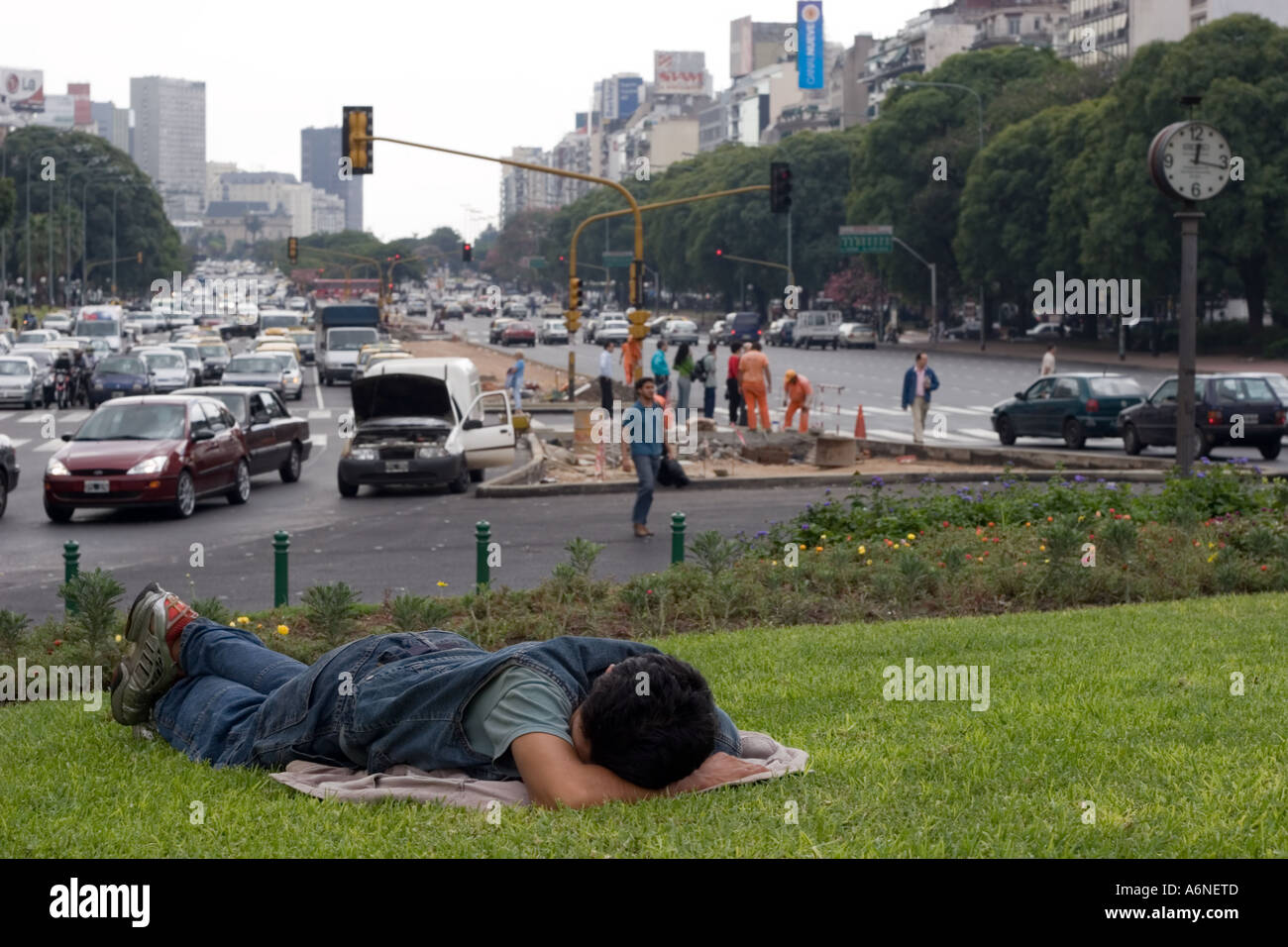 Homeless man sleeping on a grass verge in the middle of Avenida 9 de Julio (B) Stock Photo