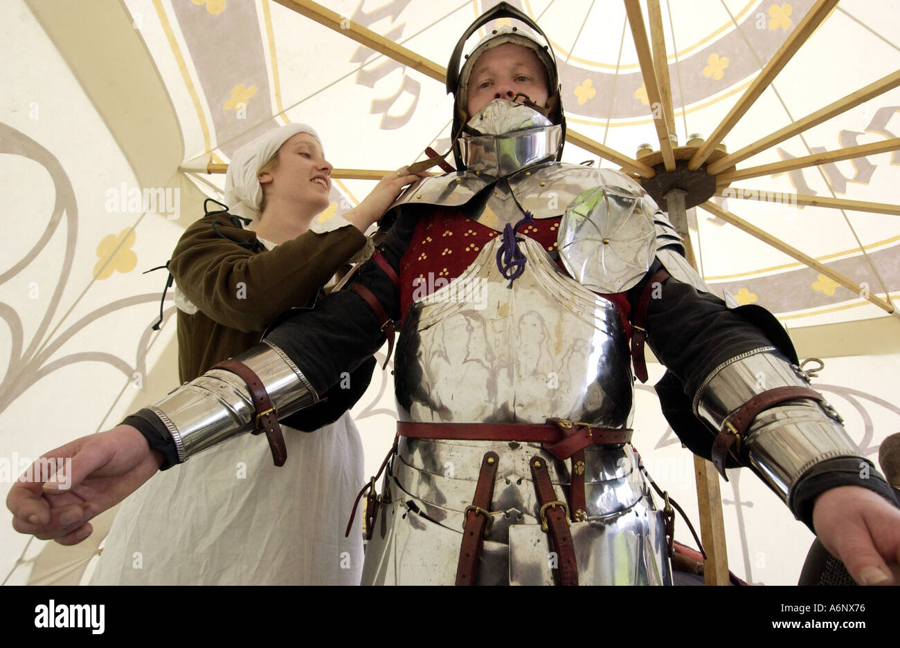 Fighting old battles. A serving wench helps dress a brave knight in his armour as part of a medieval tournament. Stock Photo