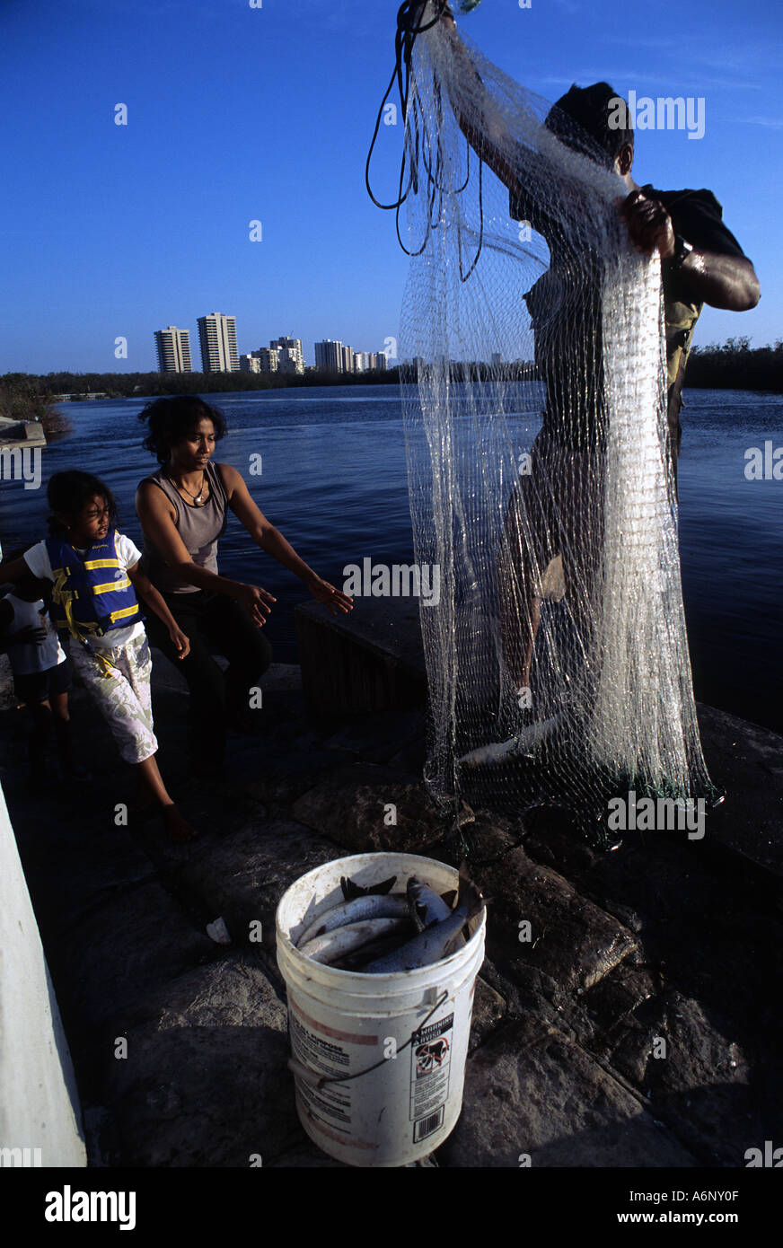 Immigrant family using castnet to catch food fish mullet in