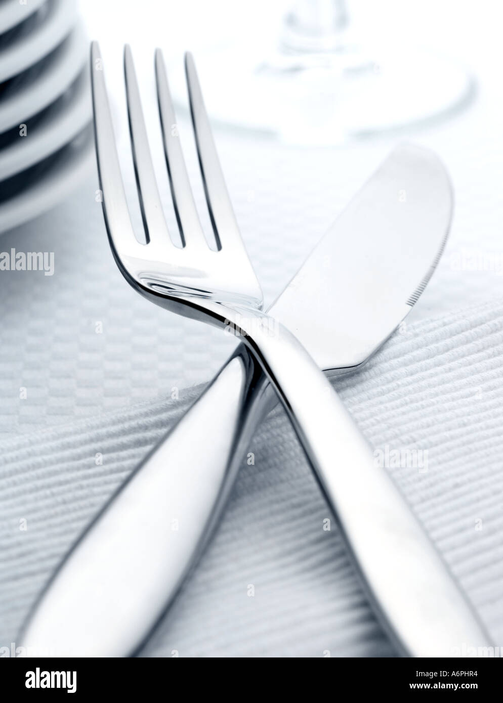 CLOSE UP OF A KNIFE AND FORK, WITH PLATES AND GLASS IN BACKGROUND Stock Photo