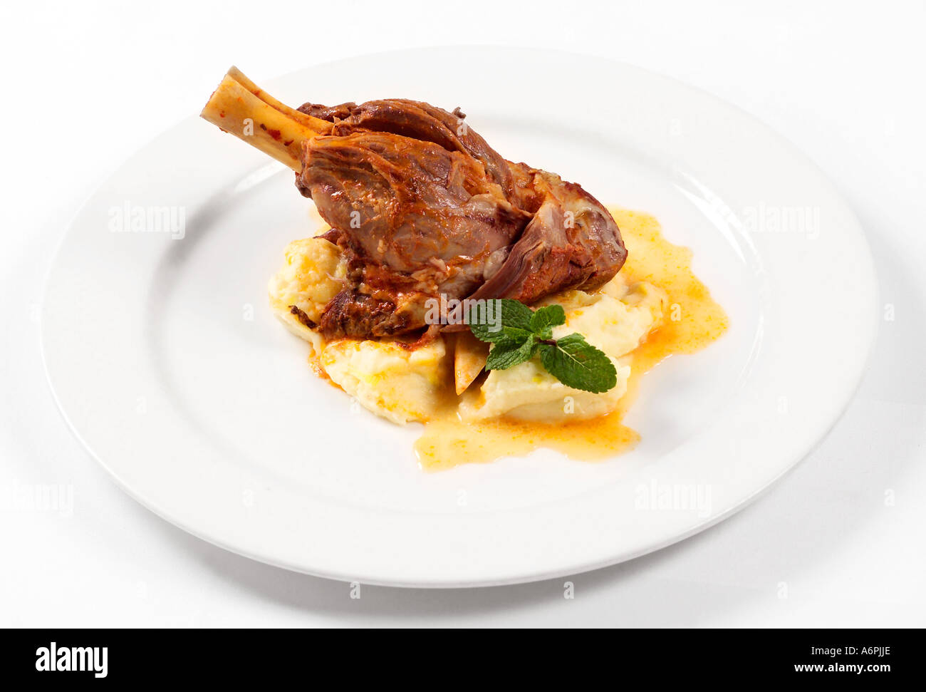 A marinated leg of lamb sitting on a bed of mash on a white plate. Stock Photo