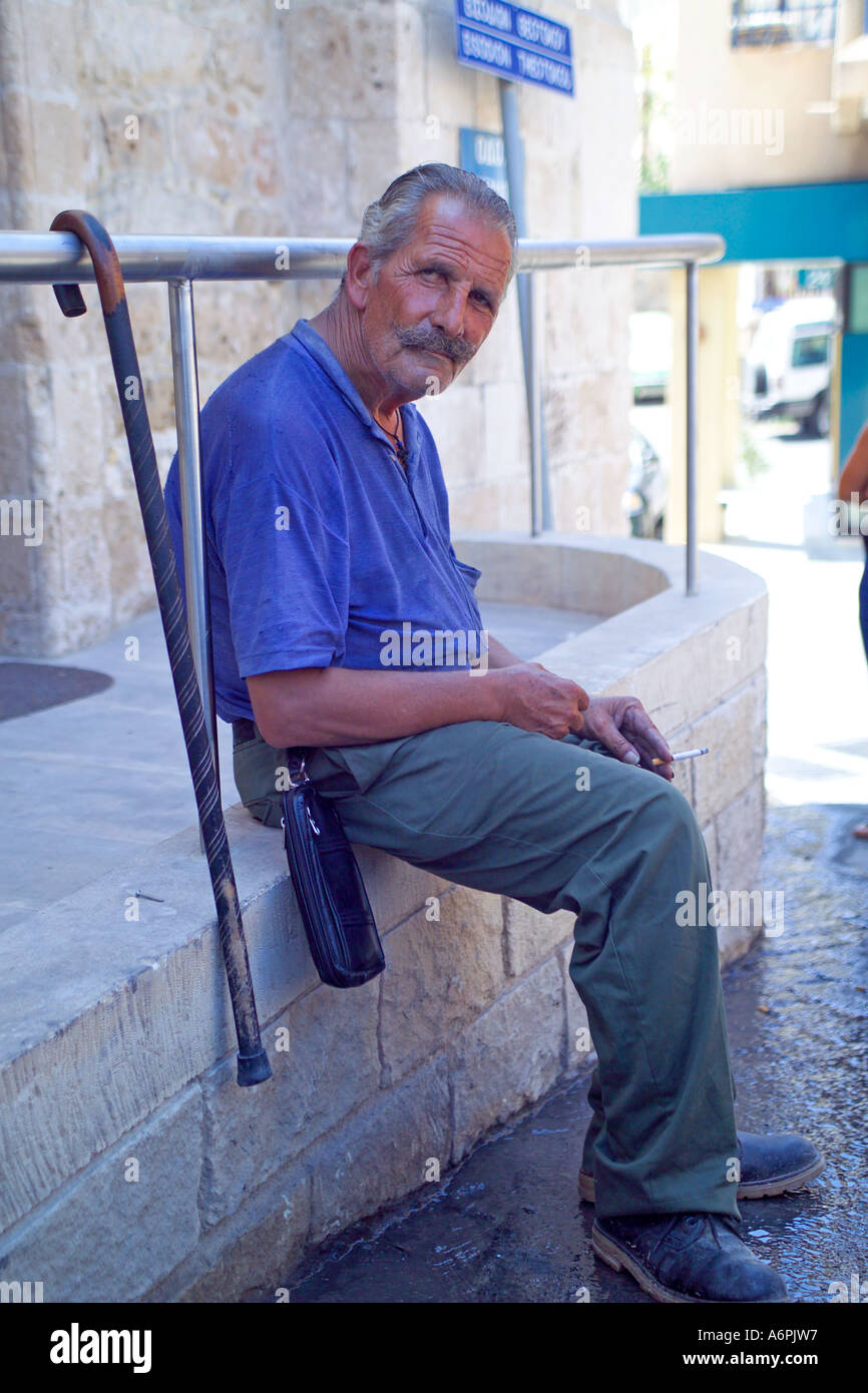 LOCAL CYPRIOT MAN SITTING ON WALL IN THE COBBLED STREET Stock Photo