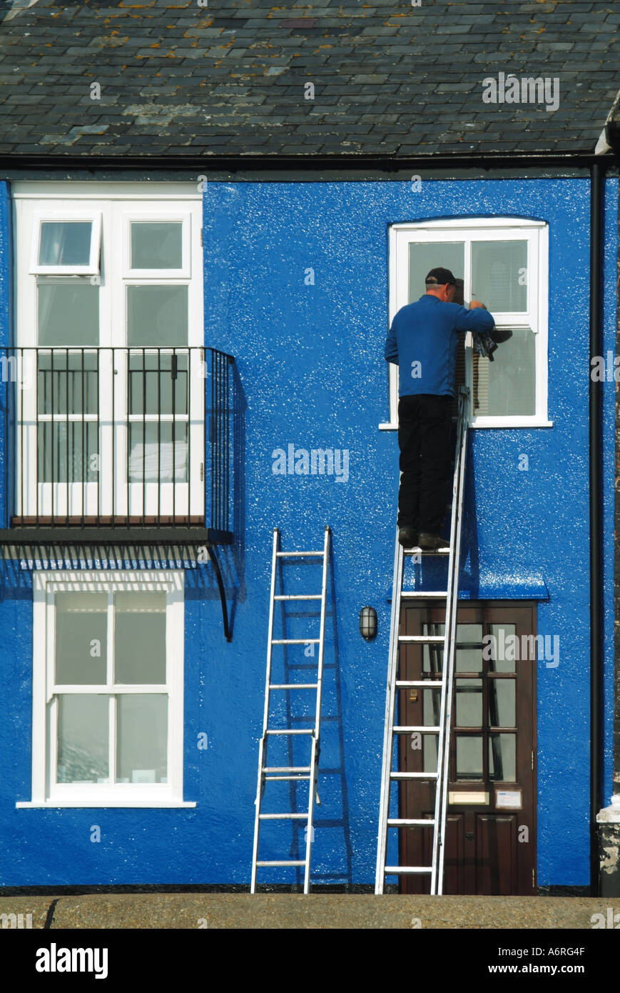 Man on ladder working on first floor window to domestic property Stock