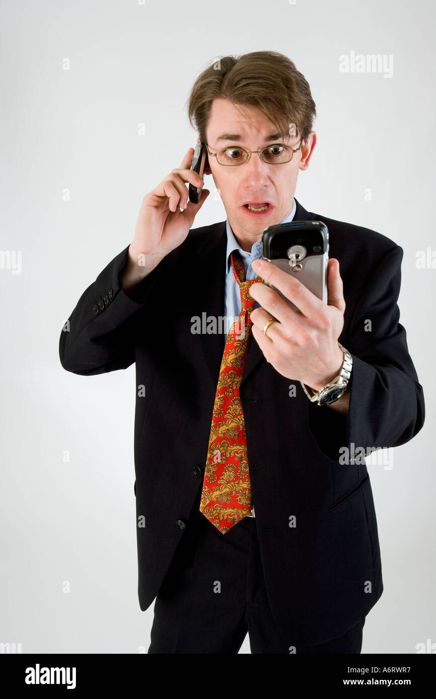 BUSINESS MAN IN DARK SUIT LOOKING STRESSED ON TALKING ON MOBILE PHONE AND HOLDING PERSONAL ORGANIZER POCKET PC Stock Photo