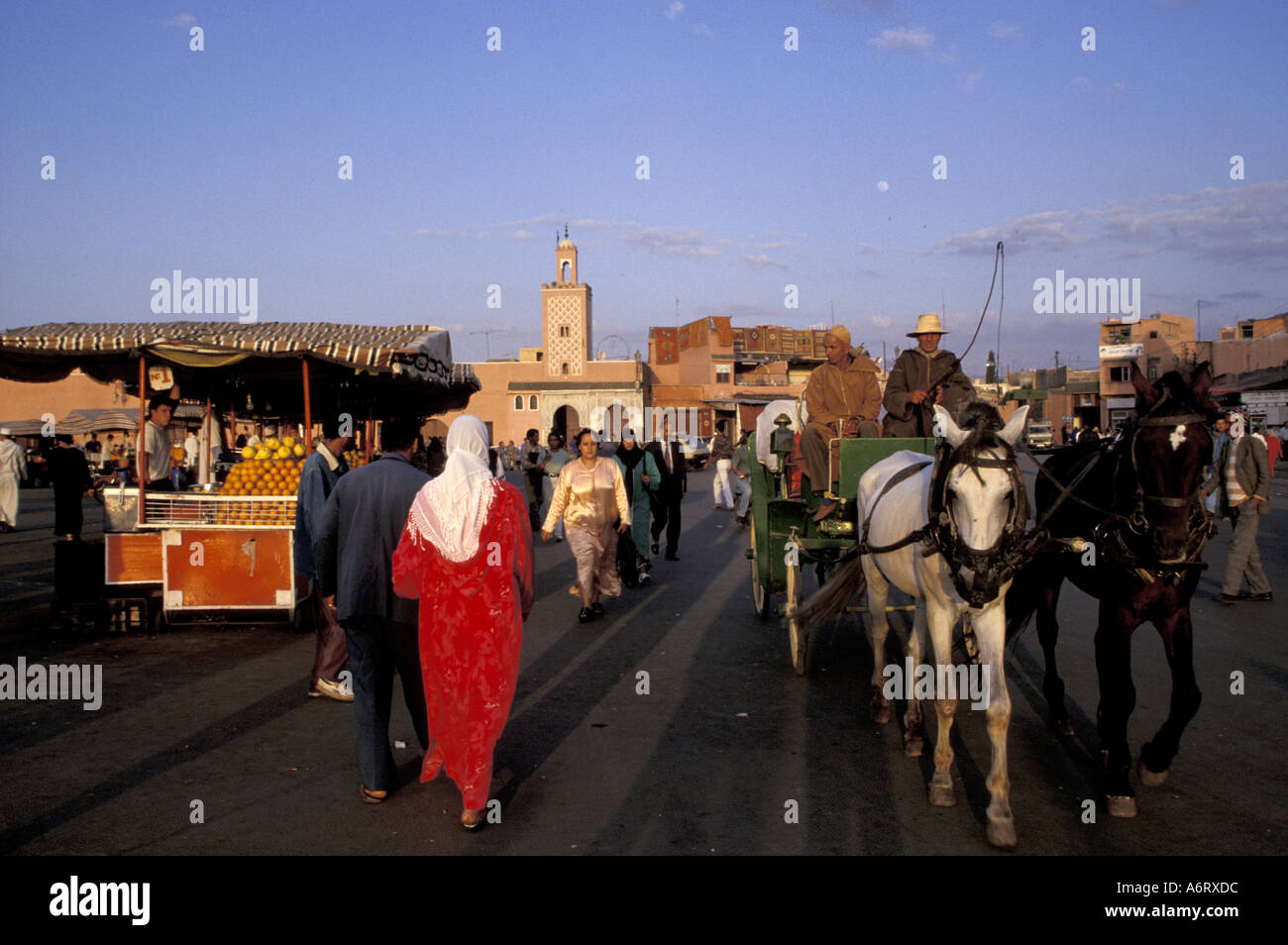 Africa, Morocco, Marrakesh, Muslims in traditional dress near orange juice stalls and mosque in Djemaa el-Fna Stock Photo