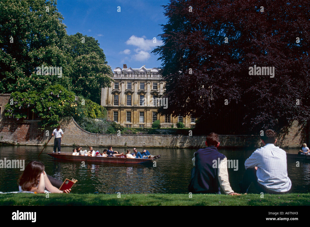 Cambridge students sitting by river Cam watching punting another student reading book Stock Photo