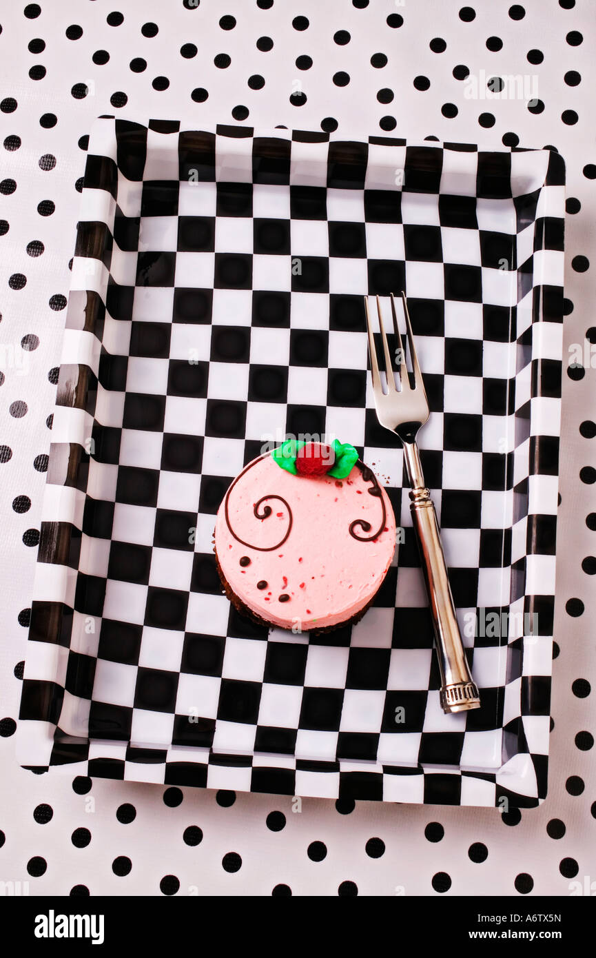 Small frosted cake in black and white  checkered tray on tablecloth of black dots Stock Photo