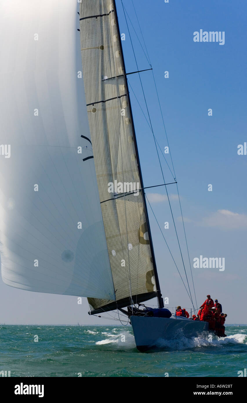 A fully crewed racing yacht with a white spinnaker catching the wind Stock Photo
