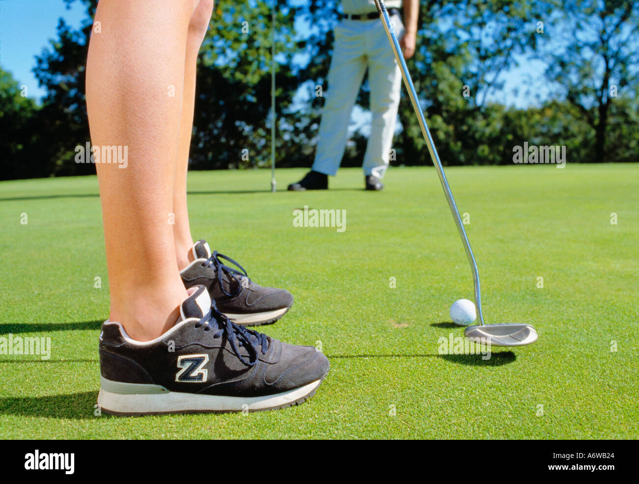 Feet of young female golfer in foreground making a putting shot Stock Photo