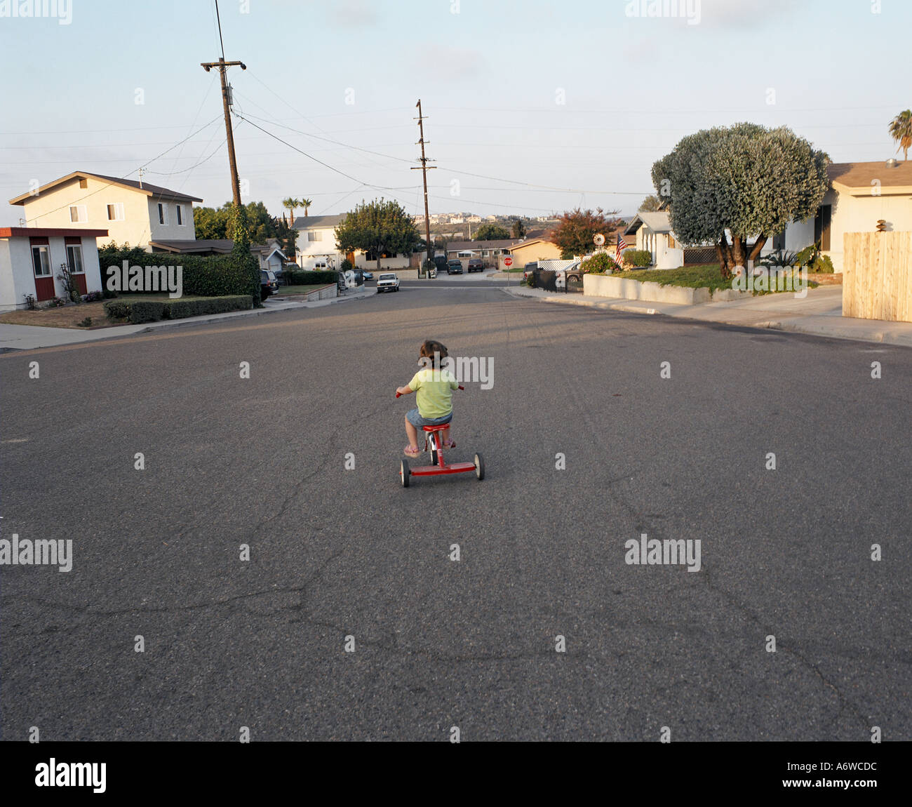 Child on red trycylce ridding down the street of a culdesac Stock Photo