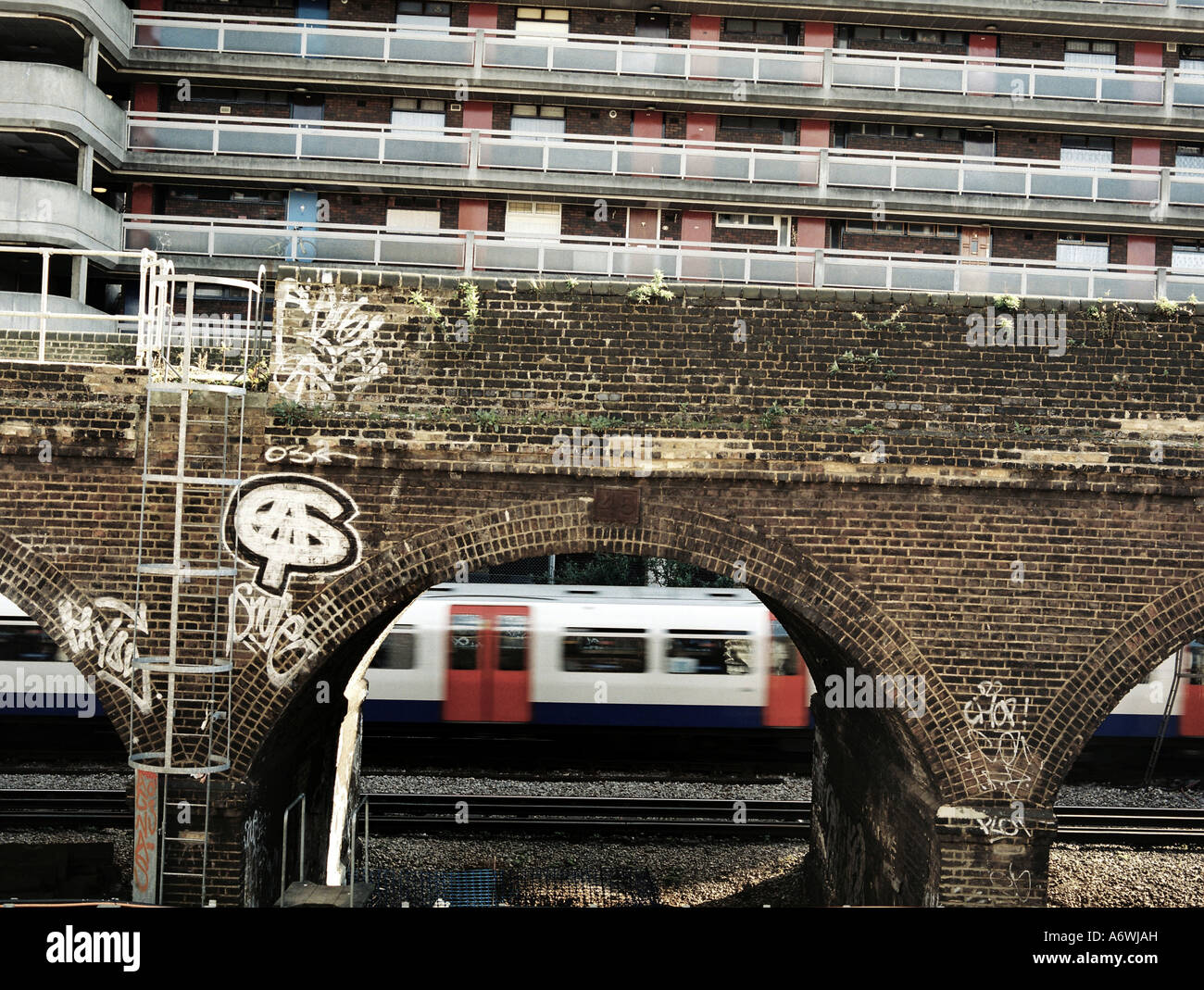 Blocks of flats above the Hammersmith Line with a red, white and blue London Underground train passing below the arches. Stock Photo