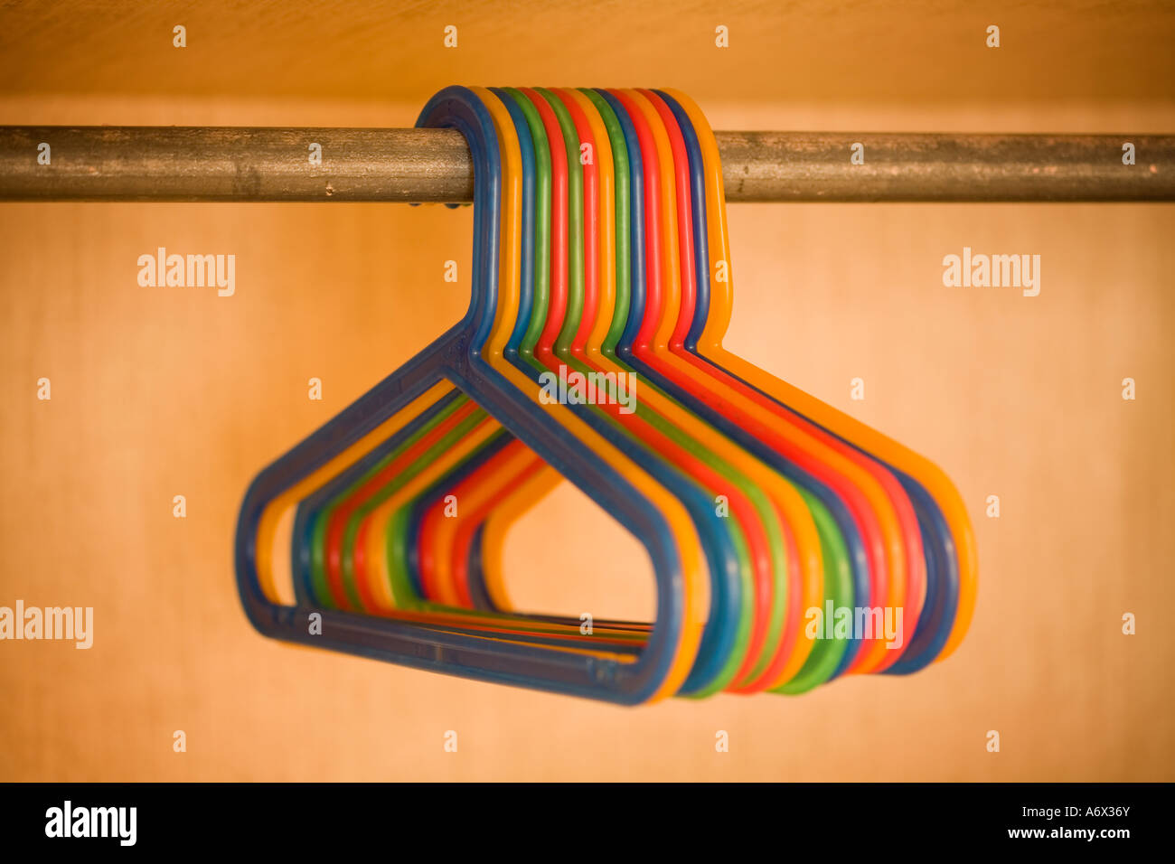 Multi colored plastic clothes hangers in closet, hanging from horizontal bar. Hangers are all very close to one another. Stock Photo