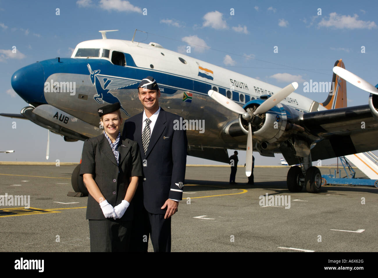 Cabin crew in traditional fifties uniforms standing alongside an old South African Airways DC-4. Stock Photo