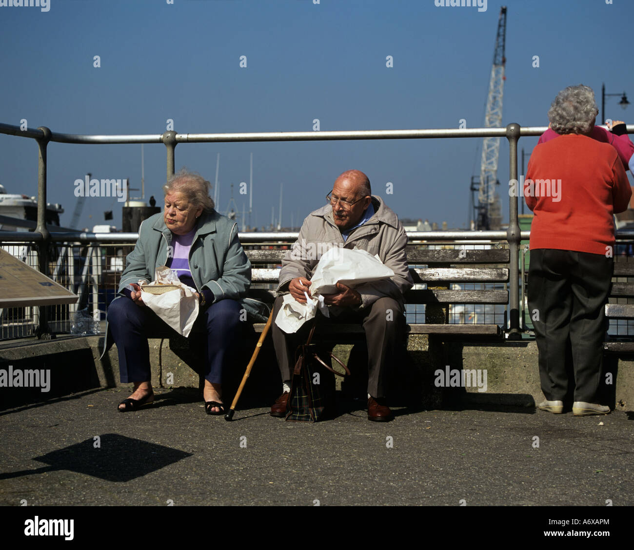 WEST SUSSEX UK March A elderly couple sitting on a bench at the harbour side enjoying a fish and chip lunch Stock Photo