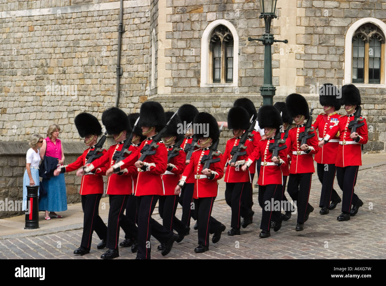 ENGLAND Windsor Changing of the Queens guard marching down cobblestone street red coats women tourists watch Stock Photo
