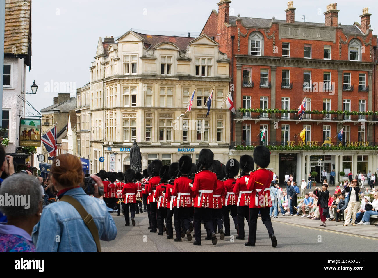 ENGLAND Windsor Changing of the Queens guard marching down street red coats and uniforms tourists stand on sidewalk watching Stock Photo