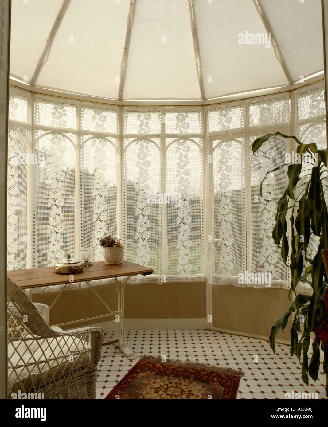 White blinds on ceiling in small conservatory with lace drapes on windows Stock Photo