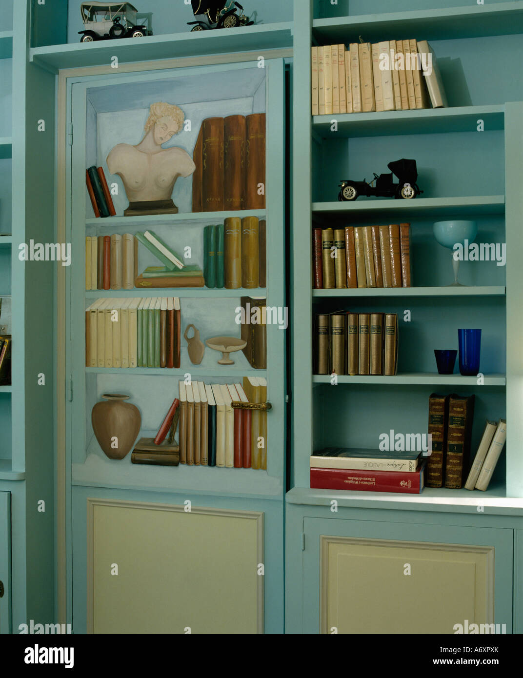 Close-up of books on blue shelves beside painted door with  trompe-l'oiel shelves Stock Photo