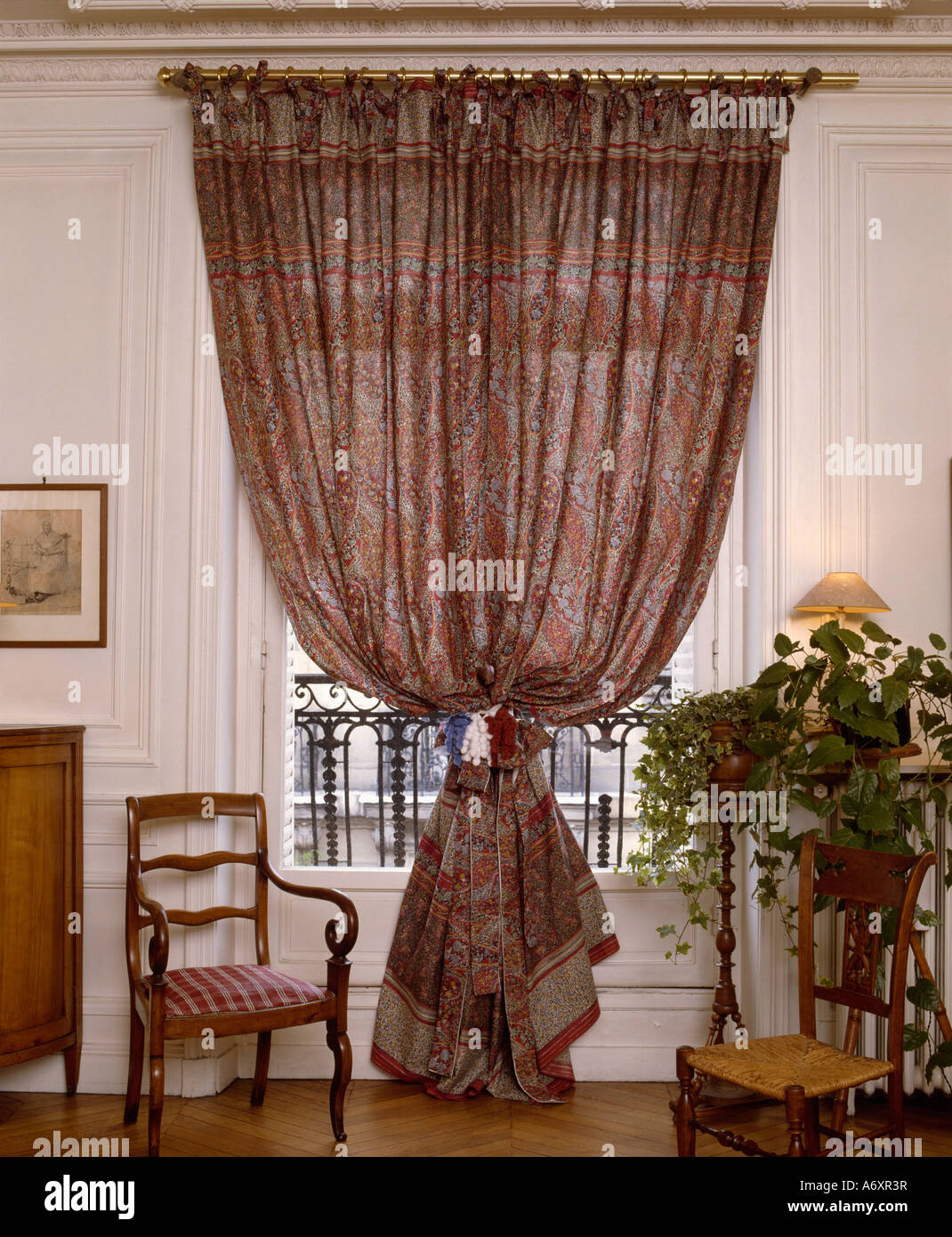 Wooden chair beside Paisley print drapes at window Stock Photo