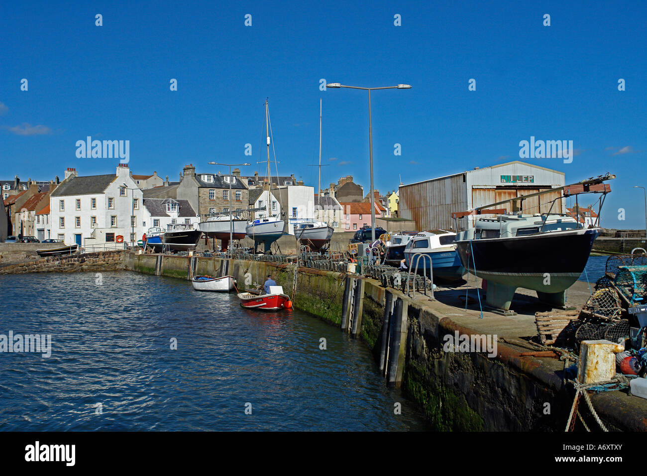 Fishing gear and boats on a pier in St. Monans harbour in Fife Scotland with traditional houses in the background. Stock Photo