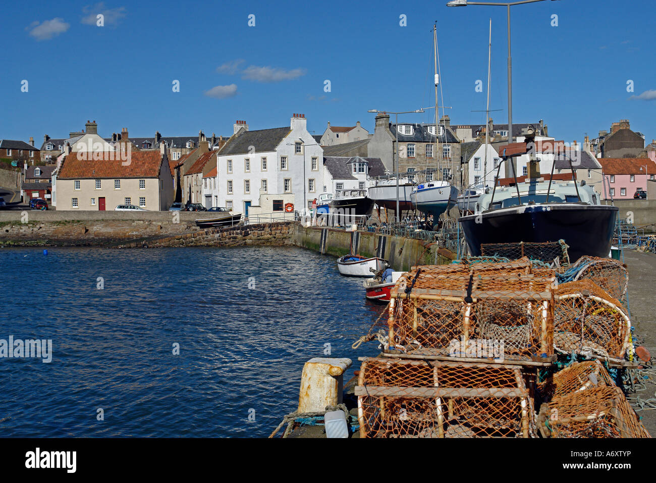 Fishing gear and boats on a pier in St. Monans harbour in Fife Scotland with traditional houses in the background. Stock Photo