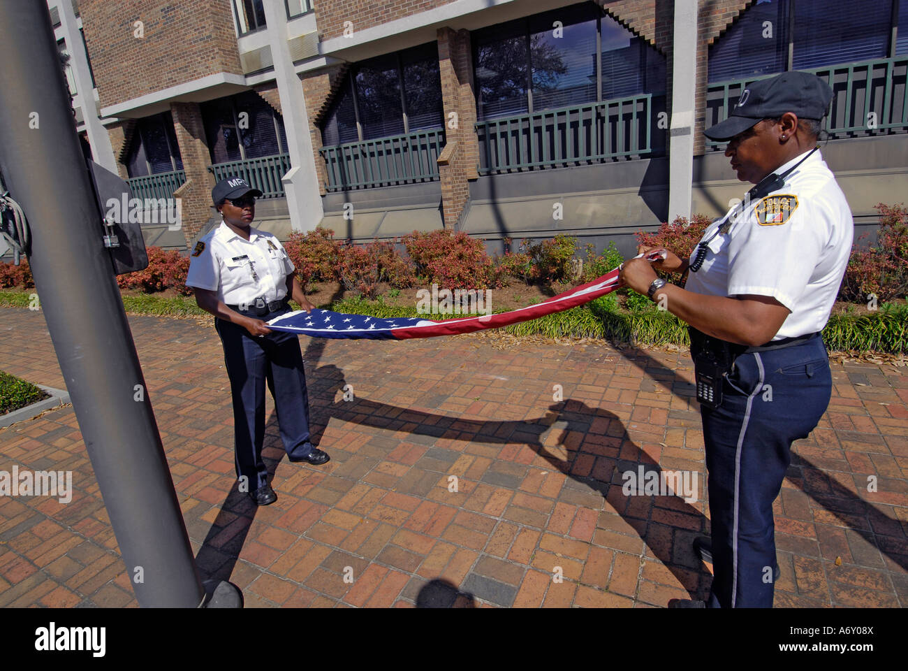 Black female police officers take the America flag down a fold it at the end of the day in Montgomery Alabama AL Stock Photo