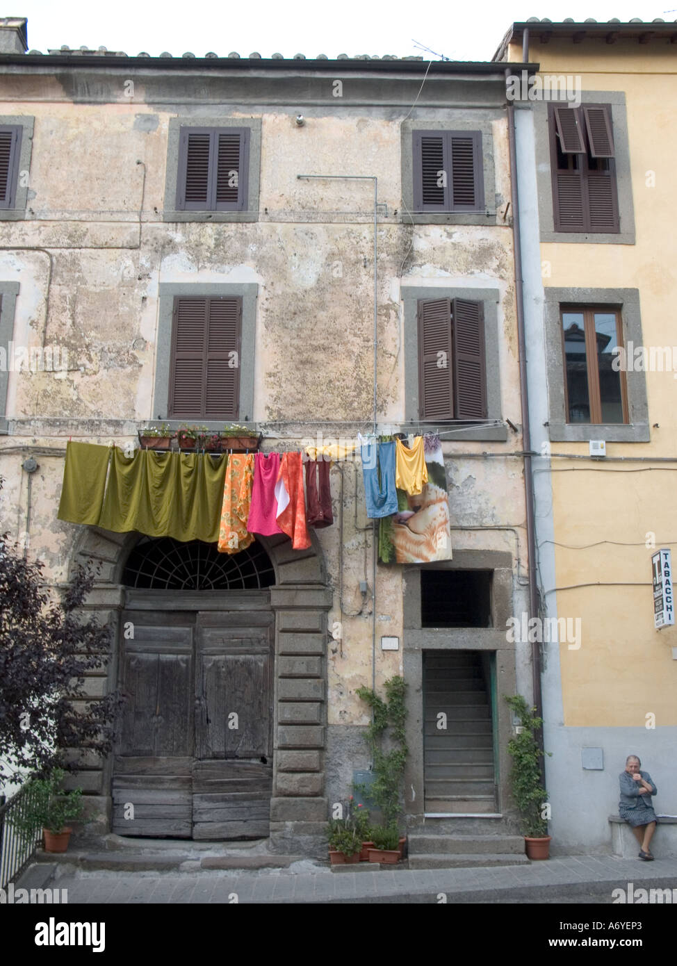 A woman sits outside passing the time of day as washing dries from a balcony in St Martino Al Cimino, Italy Stock Photo