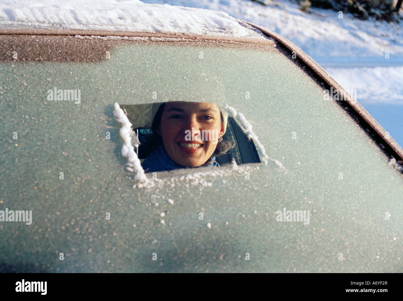 Woman sitting in car a and peeking through a frost covered ...