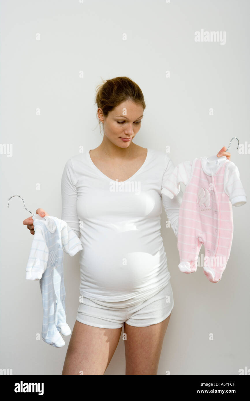 Pregnant woman holding up blue and pink baby outfits Stock Photo - Alamy