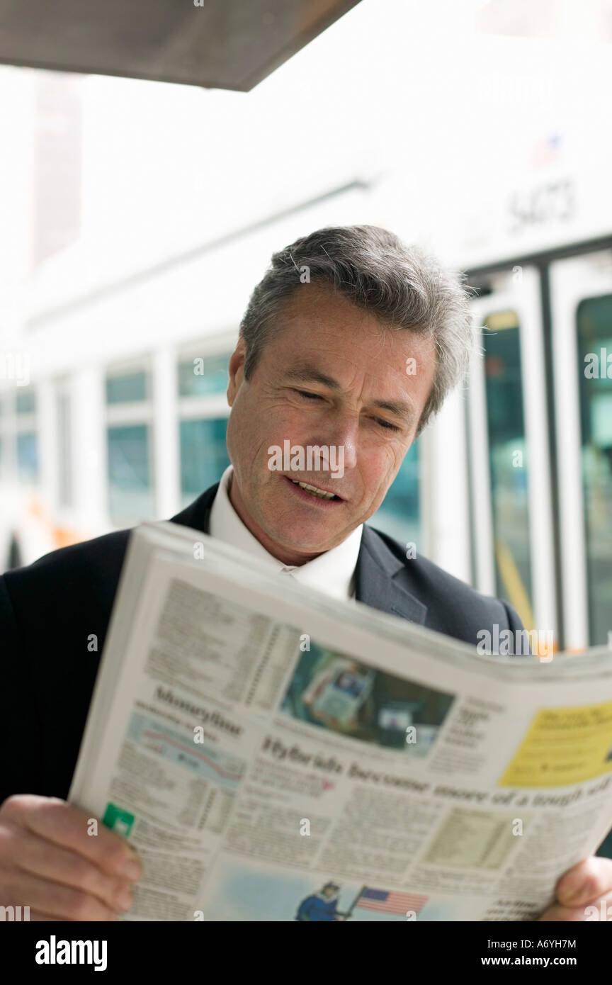 Businessman reading a newspaper at a bus stop Stock Photo